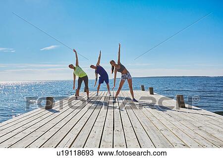 Friends on pier side by side arms raised bending over sideways stretching View Large Photo Image Stock Image - Friends on pier side by side arms raised bending over sideways stretching. Fotosearch