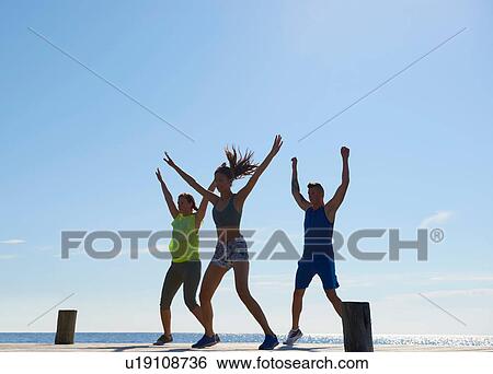 Friends on pier wearing exercise clothes arms raised exercising View Large Photo Image Stock Photograph - Friends on pier wearing exercise clothes arms raised exercising. Fotosearch