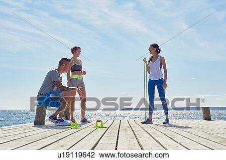 Stock Image - Friends wearing sports clothes on pier with exercise equipment. Fotosearch