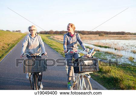 Stock Image - Front view of women cycling on path by marshland smiling. Fotosearch