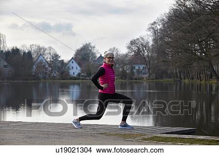 Full length side view of woman in front of pond lunging, looking at camera smiling View Large Photo Image Picture - Full length side view of woman in front of pond lunging, looking at camera smiling. Fotosearch
