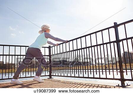 Stock Photo - Full length side view of woman leaning against railing stretching. Fotosearch