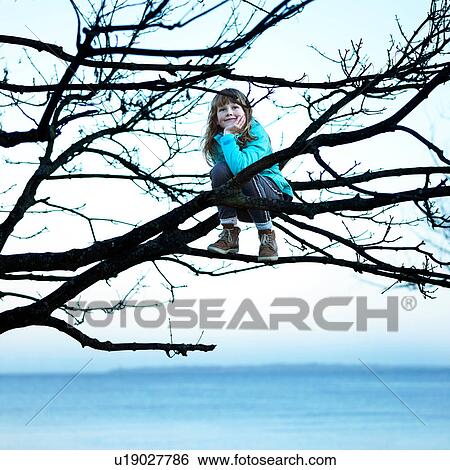 Stock Photograph - Girl in tree by ocean sitting on branch, hand on chin looking away. Fotosearch