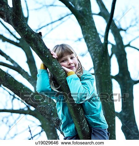 Stock Photograph - Girl in tree leaning against branch looking at camera. Fotosearch