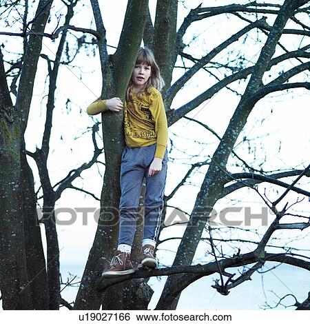 Stock Photograph - Girl in tree standing on branch looking at camera. Fotosearch