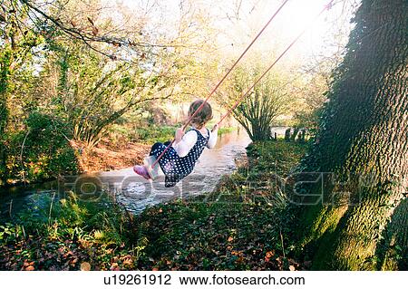 Stock Image - Girl playing swing by stream, Dorset. Fotosearch