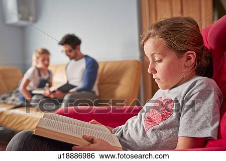 Stock Photograph - Girl, sister and father concentrating on reading books in living room. Fotosearch