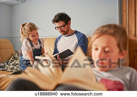 Stock Image - Girl, sister and father reading books in living room. Fotosearch