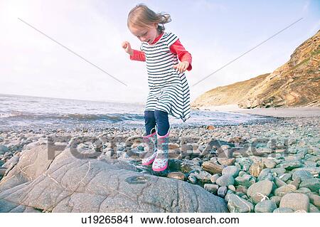 Stock Image - Girl walking on pebbles, Millook Beach, Cornwall. Fotosearch