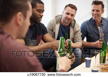 Stock Image - Group of men sitting holding beer bottles smiling. Fotosearch