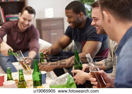 Stock Photography - Group of men sitting in lounge holding beer bottles smiling. Fotosearch