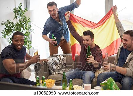 Stock Image - Group of men watching sporting event on television holding Spanish flag celebrating. Fotosearch