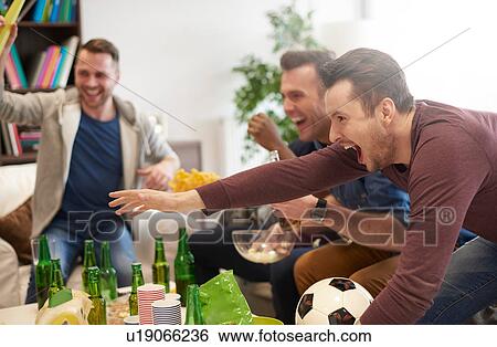 Group of men watching sporting event on television holding football celebrating View Large Photo Image Stock Photograph - Group of men watching sporting event on television holding football celebrating. Fotosearch