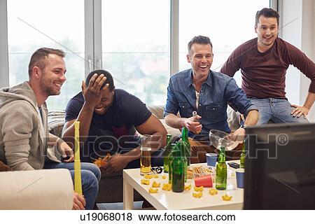 Stock Photo - Group of men watching sports event on television with snacks and beers smiling. Fotosearch
