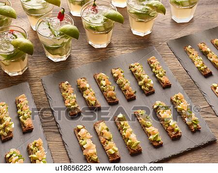 Stock Image - Guacamole, smoked salmon and rye bread canapes with vodka cocktail garnished with lime wedges. Fotosearch