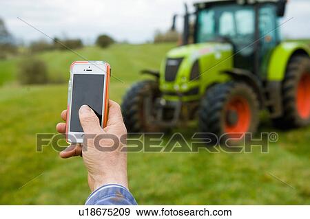 Stock Photo - Hand of farmer photographing tractor on smartphone. Fotosearch
