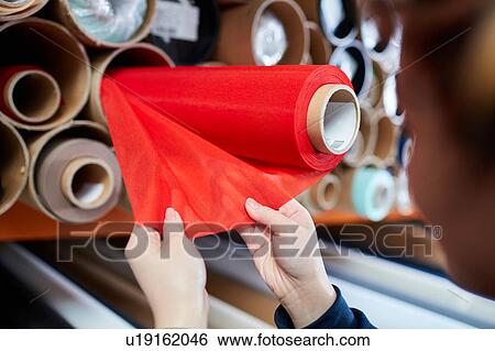 Stock Photograph - Hands of female worker examining red fabric for roller blind in factory. Fotosearch