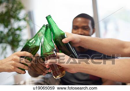 Stock Photo - Hands of group of men making a toast with beer bottles. Fotosearch