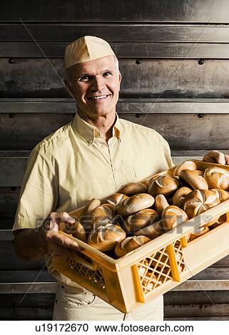 Stock Image - Happy baker carrying crate of bread rolls. Fotosearch