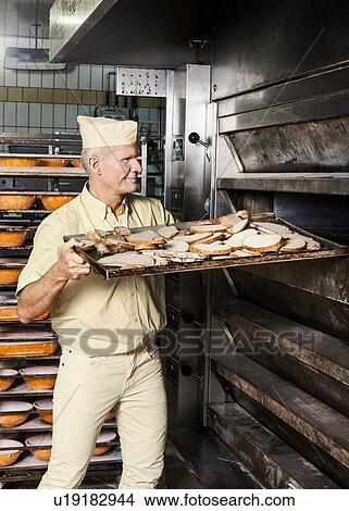 Happy baker placing tray of sliced bread into oven View Large Photo Image Picture - Happy baker placing tray of sliced bread into oven. Fotosearch