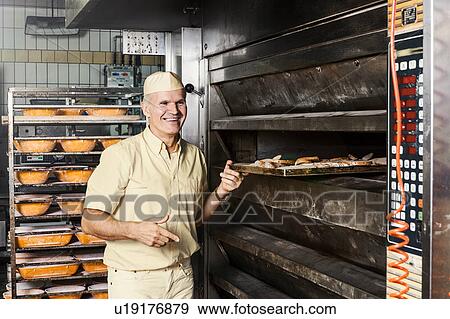Stock Photo - Happy baker placing tray of sliced bread into oven. Fotosearch