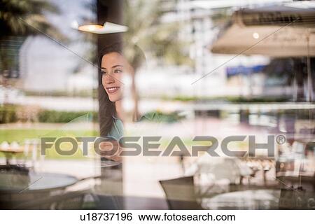 Stock Photograph - Happy woman behind reflective cafe window, Dubai, United Arab Emirates. Fotosearch