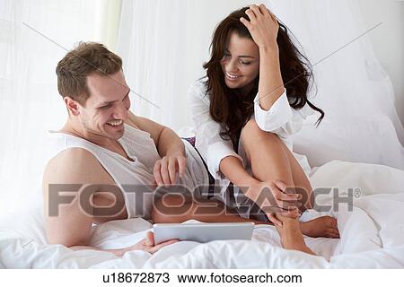 Stock Image - Happy young couple browsing digital tablet on bed. Fotosearch