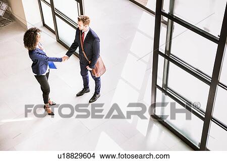 High angle view of businessman and woman shaking hands at office entrance View Large Photo Image Picture - High angle view of businessman and woman shaking hands at office entrance. Fotosearch