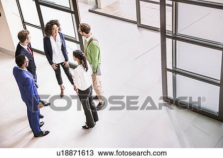 Stock Image - High angle view of businessmen and women having discussion at office entrance. Fotosearch