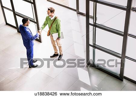 Stock Photograph - High angle view of businessmen shaking hands at office entrance. Fotosearch