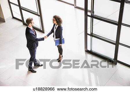 Stock Photograph - High angle view of businesswoman and man shaking hands at office entrance. Fotosearch