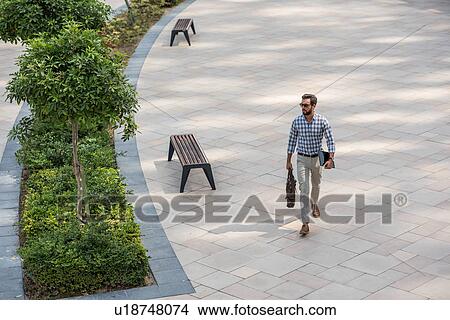 Picture - High angle view of young man walking in city carrying digital tablet, Dubai, United Arab Emirates. Fotosearch