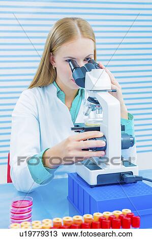 Stock Image - Lab assistant using microscope. Fotosearch