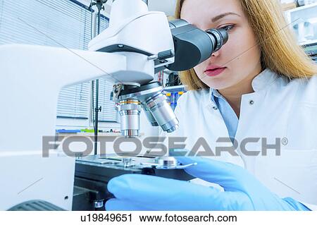 Stock Image - Lab technician using microscope. Fotosearch
