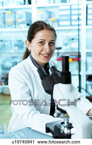 Stock Image - Lab technician with a microscope. Fotosearch