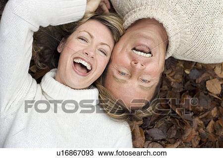 Stock Image - Laughing couple lying on autumn leaves. Fotosearch