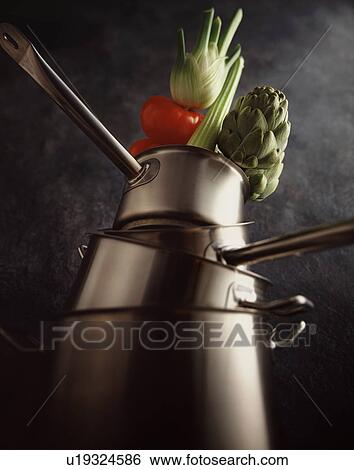 Stock Photograph - Low angle view of beef tomatoes, fennel, artichoke and celery on top of metal saucepans. Fotosearch