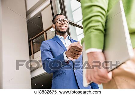 Stock Photography - Low angle view of businessmen shaking hands outside office building. Fotosearch