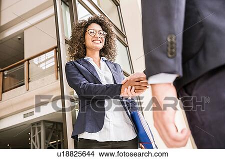 Picture - Low angle view of businesswoman shaking hands with businessman at office. Fotosearch