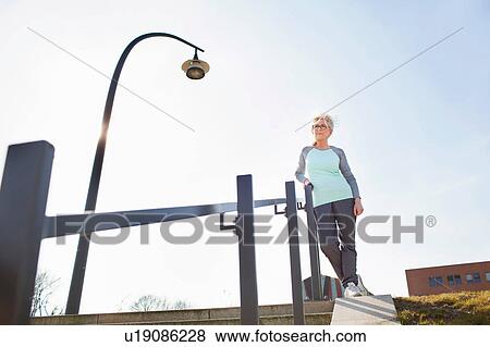 Stock Photo - Low angle view of woman leaning against banister on steps looking away. Fotosearch