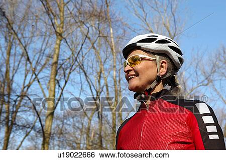 Stock Photograph - Low angle view of woman wearing cycling helmet and sunglasses looking away smiling. Fotosearch