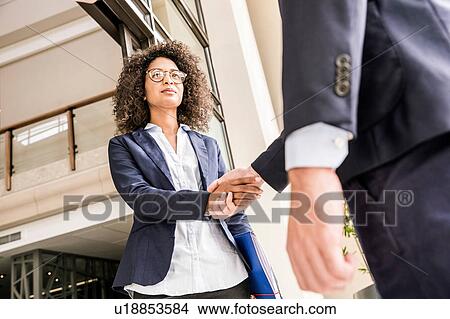 Picture - Low angle view of young businesswoman shaking hands with businessman at office. Fotosearch