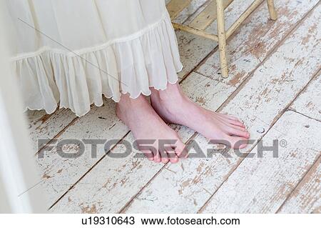 Stock Image - Low section of woman standing barefoot on white washed floorboards. Fotosearch