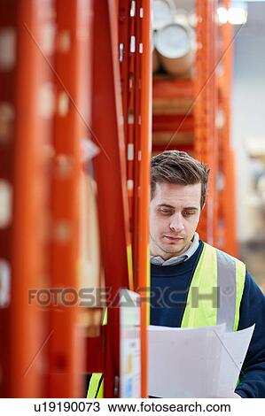 Stock Image - Male factory worker checking paperwork in factory warehouse. Fotosearch