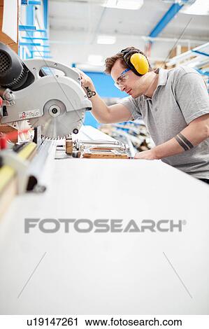 Stock Image - Male factory worker using circular saw in roller blind factory. Fotosearch