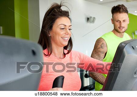 Man and woman in gym using exercise machine smiling View Large Photo Image Stock Photo - Man and woman in gym using exercise machine smiling. Fotosearch