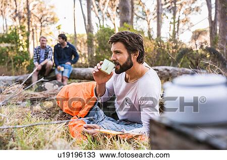 Stock Image - Man in sleeping bag drinking coffee, Deer Park, Cape Town, South Africa. Fotosearch