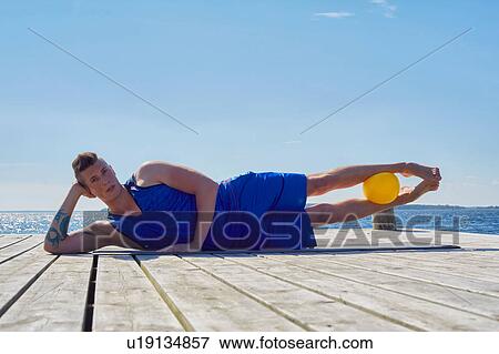 Man lying on side on pier, resting on elbow ball between legs looking at camera View Large Photo Image Stock Photo - Man lying on side on pier, resting on elbow ball between legs looking at camera. Fotosearch