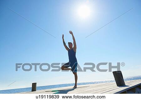 Man on pier standing on one leg arms raised exercising View Large Photo Image Stock Photo - Man on pier standing on one leg arms raised exercising. Fotosearch