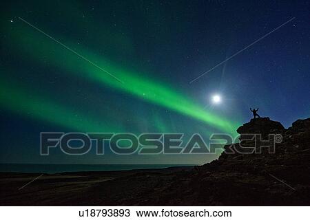 Stock Image - Man standing on rocks, watching Northern Lights, Krysuvik, Iceland. Fotosearch